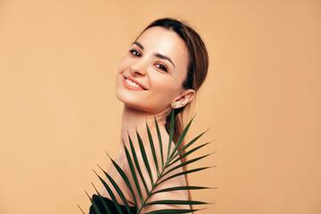 Beauty portrait of amazing gorgeous beautiful brunette woman. Serious model posing naked. Female isolated over beige wall background with green nature leaf plant. Cheerful and happy