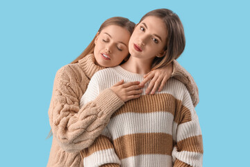 Poster - Young lesbian couple in warm sweaters hugging on blue background