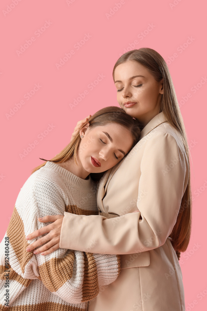 Young lesbian couple hugging on pink background