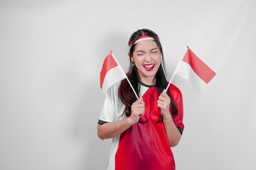 Excited young Indonesian woman wearing jersey is holding flags watching sport match competition.