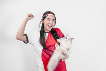 Wall Mural - Smiling Indonesian woman wearing jersey is holding a white ragdoll pet cat while raising fist.