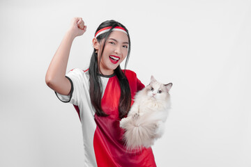 Smiling Indonesian woman wearing jersey is holding a white ragdoll pet cat while raising fist.