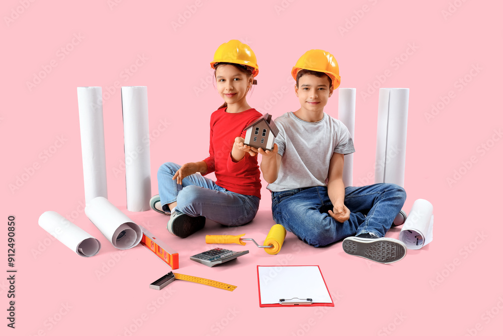 Little architects with house model and supplies sitting on pink background