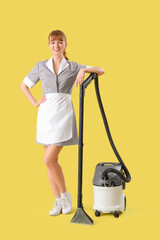 Canvas Print - Young chambermaid with vacuum cleaner on yellow background