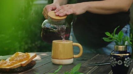 Wall Mural - Outdoor tea party. Woman pouring red hibiscus tea into mug on wooden table.