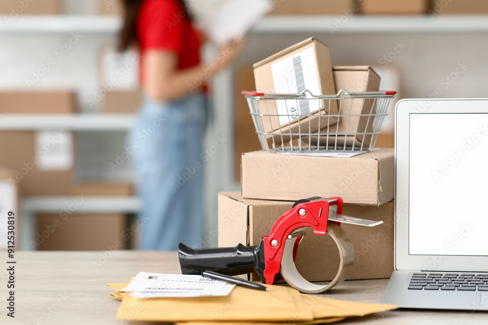 Shopping basket with parcel boxes and packing tape dispenser on table at postal warehouse, closeup