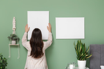 Wall Mural - Young woman hanging empty canvas on green wall in bedroom. Back view