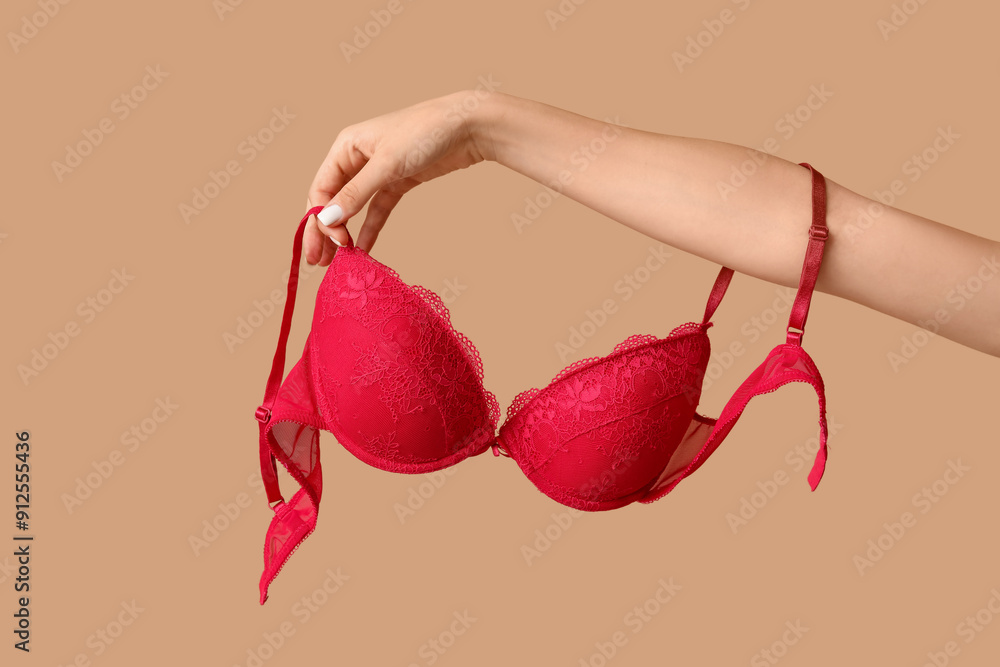 Female hands with stylish lace bra on beige background, closeup