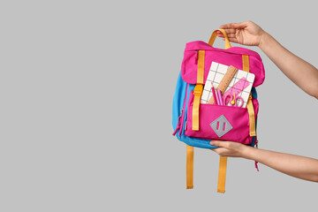 Wall Mural - Female hands with backpack and different school supplies on grey background, closeup