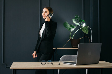 Wall Mural - Confident businesswoman using her smartphone in a modern office. Ideal for themes of professional communication, business technology, and corporate success.