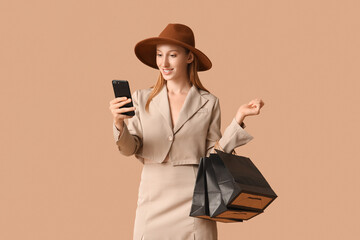 Poster - Young woman in autumn clothes with mobile phone and shopping bags on brown background