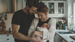 © GraysonStock - Family happiness, a young family cuddling their baby in the kitchen at home.