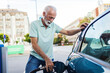 © Jelena Stanojkovic - Cheerful mature businessman filling up car tank with fuel at gas station. Happy mid adult man refueling his car the gas station.