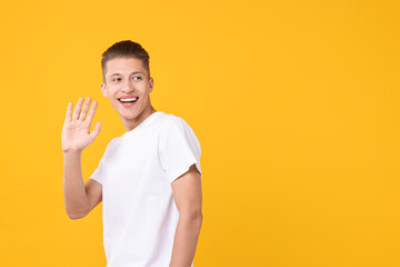 Poster - Goodbye gesture. Happy young man waving on orange background, space for text