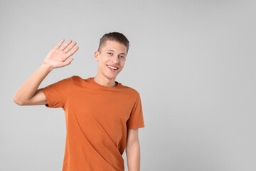 Poster - Goodbye gesture. Happy young man waving on light grey background, space for text