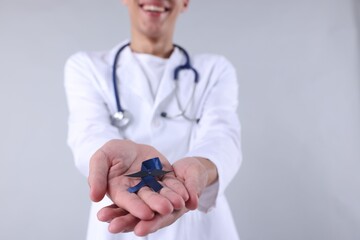 Sticker - Prostate cancer awareness. Doctor holding blue ribbon with fake mustache on light grey background, selective focus