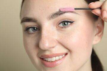 Sticker - Young woman with spoolie brush on beige background, closeup. Eyebrow correction