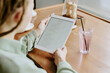 © AnnaStills - Person holding tablet reviewing digital menu in cozy bistro while drinking refreshment. Hands gripping device revealing tranquil dining setting with glass of beverage