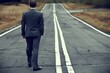 © tienuskin - A man in a business suit walking down an empty road with double yellow lines.