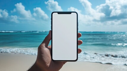 Close-up of a hand holding a smartphone with a blank white screen, beach in the background. Ideal for app promotions and digital marketing.