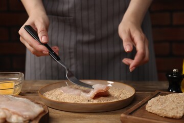 Wall Mural - Woman making schnitzel at wooden table, closeup