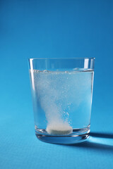 Wall Mural - Effervescent pill dissolving in glass of water on light blue background