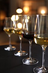 Wall Mural - Different tasty wines in glasses on black table against blurred lights, closeup