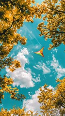 Canvas Print - Kite flying through blue sky with yellow leaves.