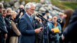 © Prostock-studio - An official delivers a speech at a coastal venue, addressing an attentive audience surrounded by photographers and onlookers during the daytime.