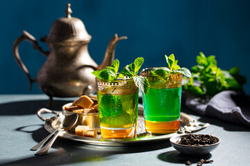 Moroccan mint tea in traditional glasses with vintage teapot on silver tray. Grey background.