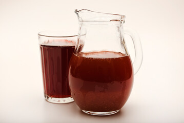 Cherry nectar in a jug and a glass on a white background.