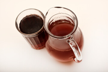 Cherry nectar in a jug and a glass on a white background.