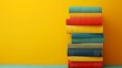 © YURY YUTY - Stack of colorful books against a vibrant yellow background.