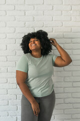 Canvas Print - Laughing millennial African American woman with an afro hairstyle and good sense of humor smiling and laugh on brick wall at home background. Copy space. Happiness and good emotions concept