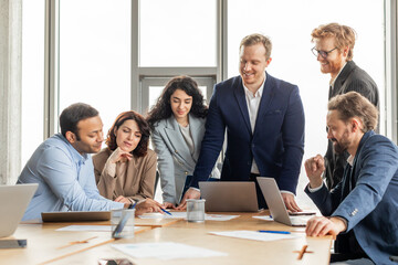 Aufkleber - A group of diverse business professionals are gathered around a table in a modern office, working together on a project. They are looking at a laptop screen and discussing ideas