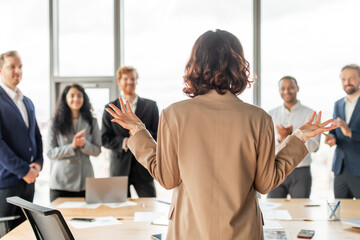 Aufkleber - A businesswoman is giving a presentation to her colleagues in a modern office. She is standing with her back to the camera and is gesturing with her hands. Her colleagues are all smiling