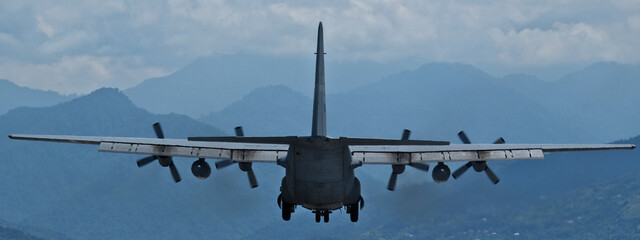 A military transport plane approaches for landing against a backdrop of mountains.