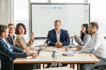 Aufkleber - A group of business professionals are gathered around a table in a modern office, discussing a growth chart displayed on a large screen. The team is engaged in a lively conversation