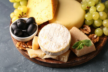 Canvas Print - Plate with different types of tasty cheese and grapes on green background, closeup