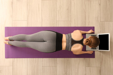 Poster - Sporty young woman with laptop doing yoga in gym, top view