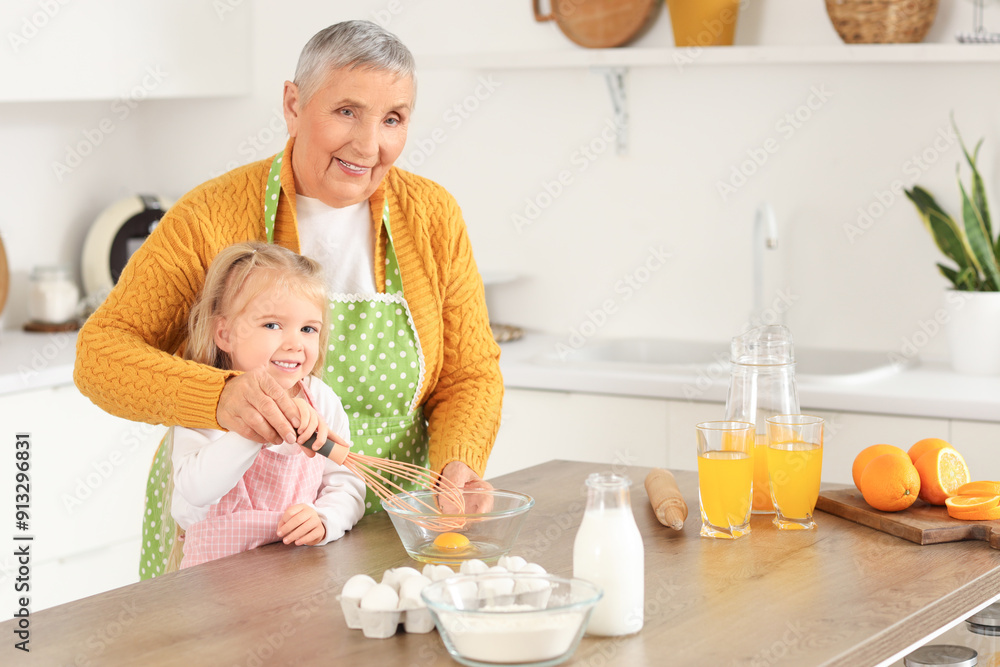 Cute little girl with her granny beating egg at table in kitchen