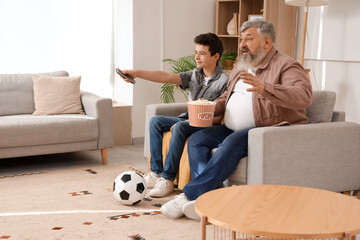 Canvas Print - Happy grandfather with his grandson watching TV and eating popcorn at home