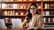 © juanorihuela - A woman is working in a library using her laptop and reading a book.