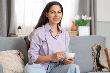 Wall Mural - Pretty young woman with cup of hot coffee sitting on sofa at home