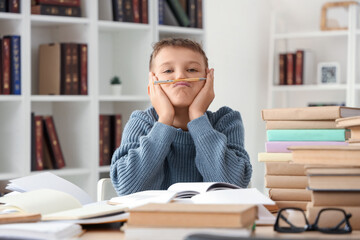 Canvas Print - Tired teenage boy with pen and books at table in library