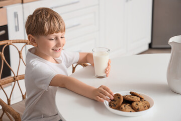 Canvas Print - Cute little boy with glass of milk and cookies sitting by table in kitchen