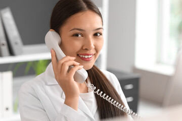 Poster - Young female medical receptionist talking on phone in hospital