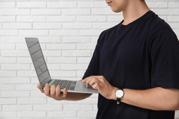 Male programmer using laptop on white brick background