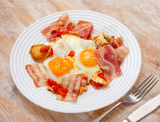 Canvas Print - Delicious homemade breakfast of fried eggs with potatoes, pieces of ripe tomatoes and crispy streaky side bacon slices..