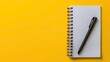 © sablengjago - A white notebook with a black pen on a yellow background.